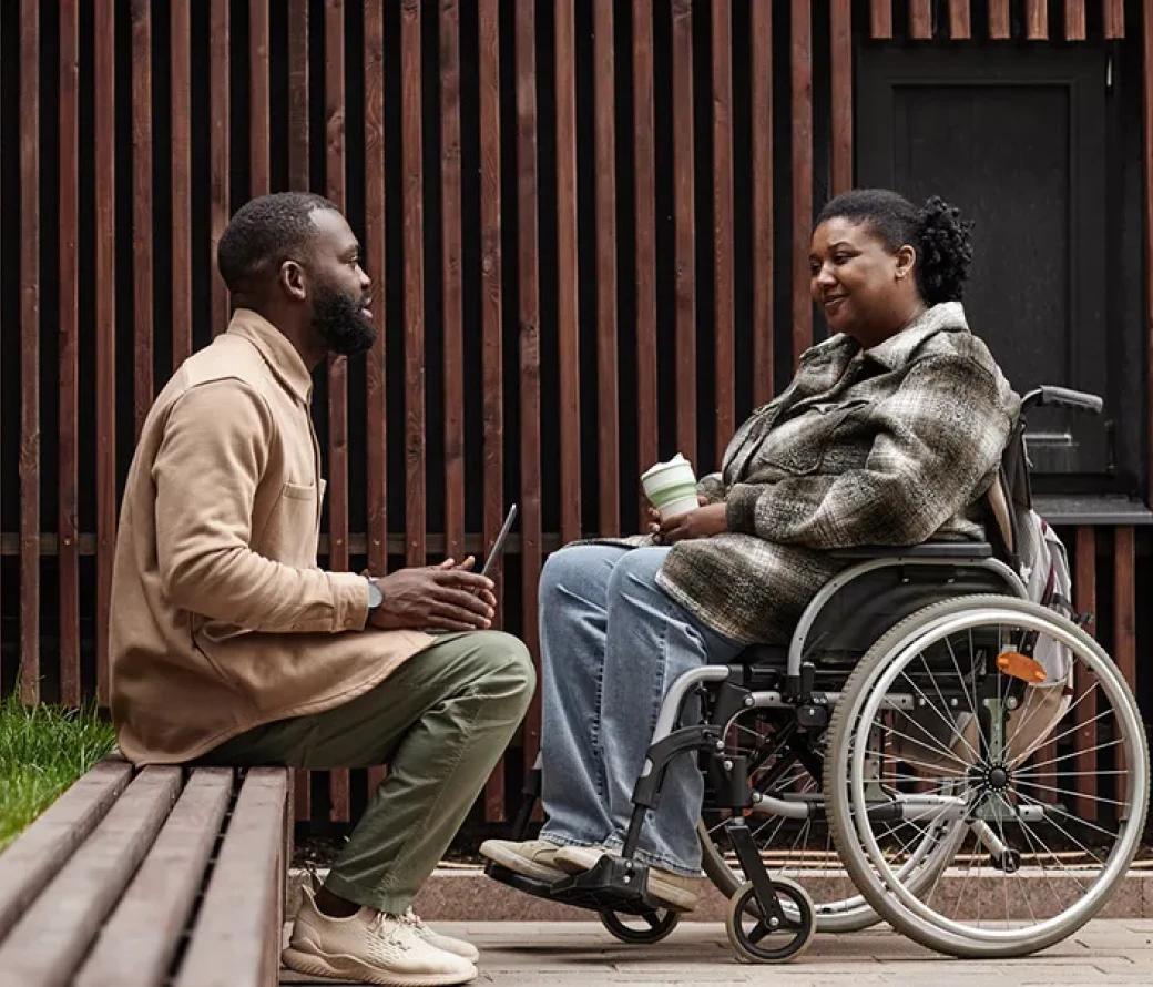 an image of two african american people talking, a man on a bench, a woman in a wheelchair